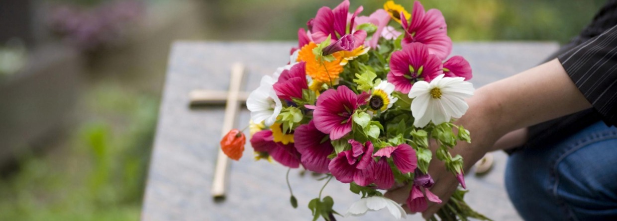 Vrouwenhand die een bos bloemen op een graf legt